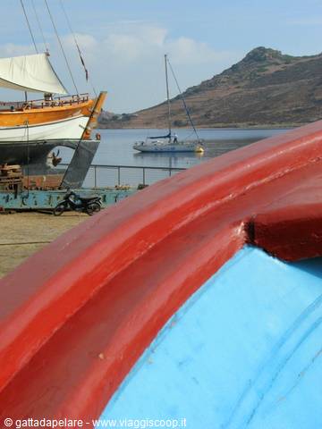 Red and blue boat bow, stranded tall ship and anchored sailboat in the bay