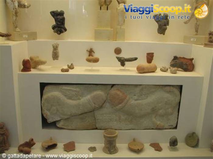 Museum display with stone relief and ancient pottery on lit shelves