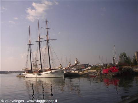 White three-masted schooner moored at the harbor next to a red tugboat