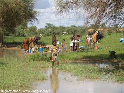 Women and children in colorful clothes collecting water from a green swamp