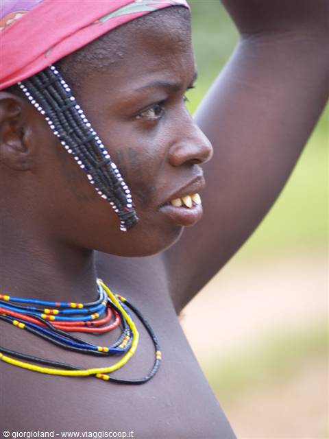 Young woman wearing colorful beaded necklaces and red headband among Mursi villages