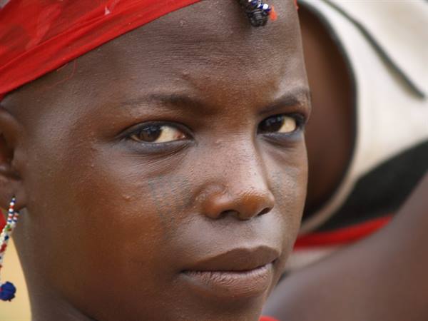 Woman in red headscarf with beaded earrings stares intently at the camera
