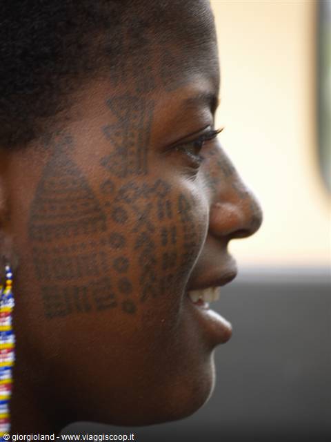 Woman's face with traditional facial scarification patterns and colorful beaded earrings