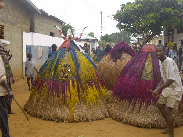 Colorful straw Zangbeto masks dance down the street among onlookers, Benin