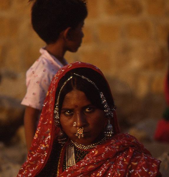 Woman in red sari with silver jewelry and nose ring beside a child by stone walls