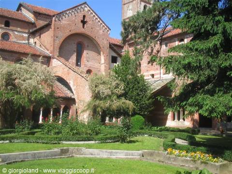 Green cloister garden before the brick Romanesque facade of Sant'Ambrogio, Milan