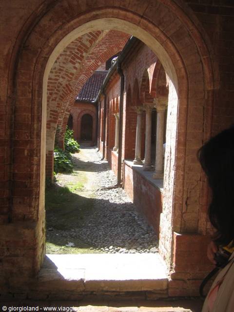Brick cloister with arches and stone columns, sunlight on the pebbled path