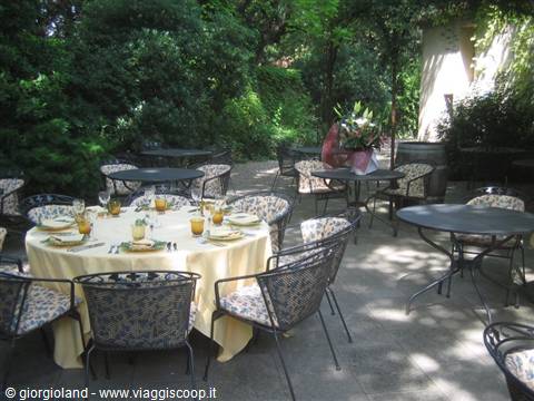 Wrought iron tables set for lunch in a shaded restaurant garden