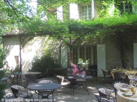 Wrought iron tables under wisteria pergola, house with green shutters