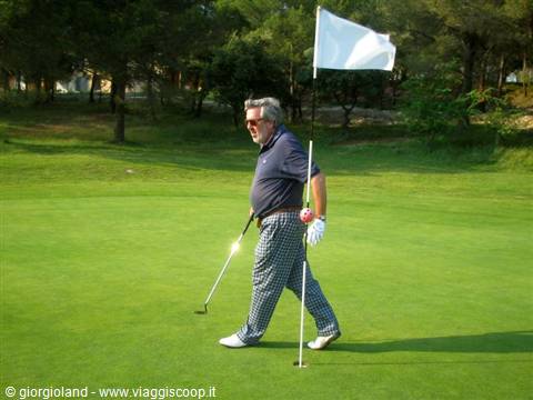 Man with putter and flagstick walks across a golf course green