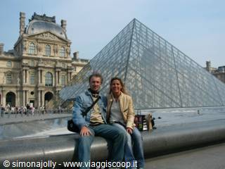 Smiling couple sitting in front of the glass Louvre pyramid in Paris