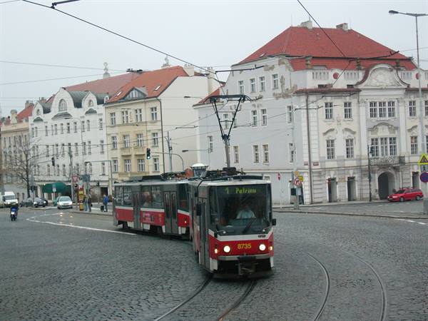 Red and white tram turning on cobblestones among historic buildings in Prague