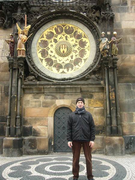 Man in black jacket before Prague's astronomical clock, golden medallions and statues