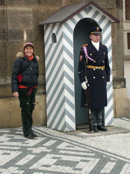 Tourist smiles beside uniformed guard under the striped sentry box, Prague