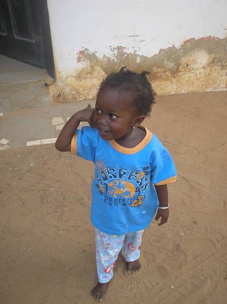Smiling little girl in blue t-shirt on sandy ground in front of weathered wall