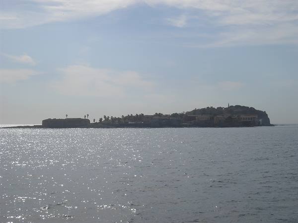 Island with buildings and palms seen from the sea, sunlight sparkling on water
