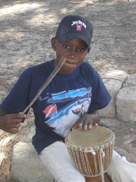 Boy in black cap plays a wooden djembe drum holding a stick