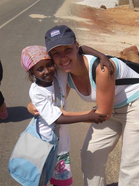 Tourist hugs a local girl with blue bag on a paved road