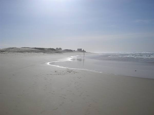 Sandy beach under haze, high sun, a person walking along the shoreline