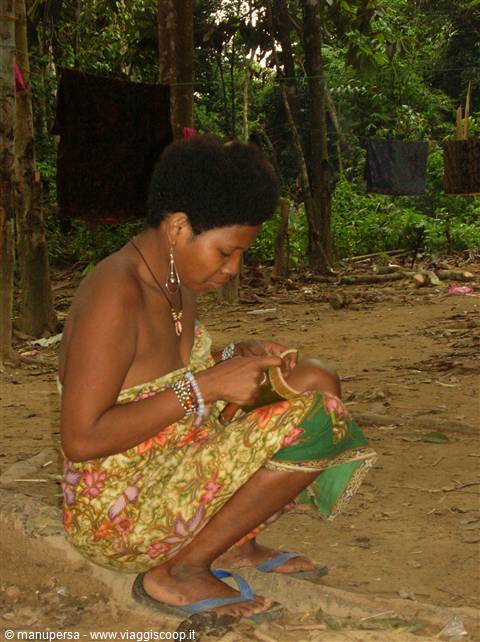 Woman crouching by a tree carves a gourd in the forest