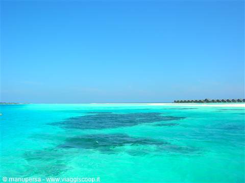 Turquoise water over coral reef, overwater bungalows on the horizon, Maldives