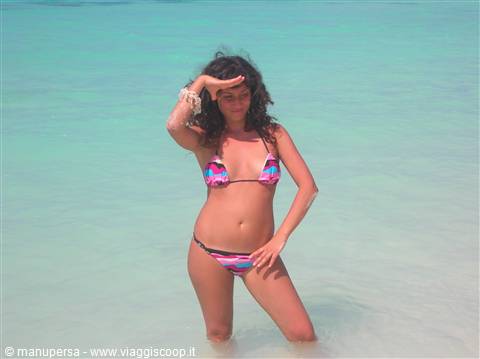 Woman in colorful patterned bikini standing in clear turquoise water, shielding eyes from sun