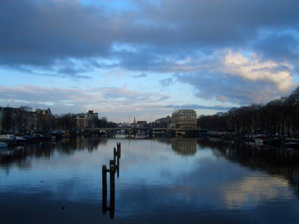 Amstel river in Amsterdam, wooden mooring poles reflected in calm water