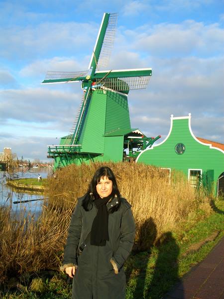 Woman in black coat in front of a green wooden windmill at Zaanse Schans