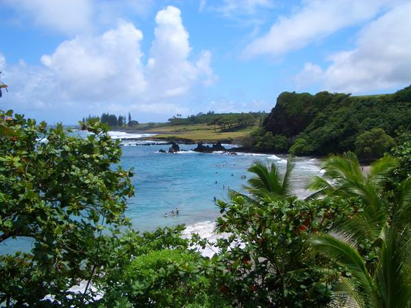 Swimmers in turquoise water at Hamoa Beach, palms and green cliffs under white clouds