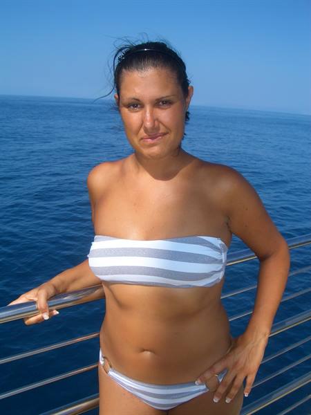 Woman in striped bikini standing on a boat, hand on chrome railing
