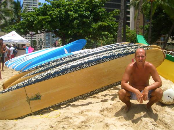 Man crouching beside wooden surfboards on the sand at Waikiki