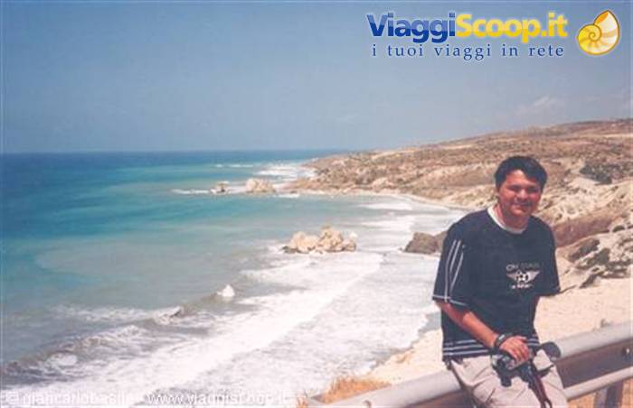 Smiling man in black shirt beside rocky coast with turquoise waves and white foam