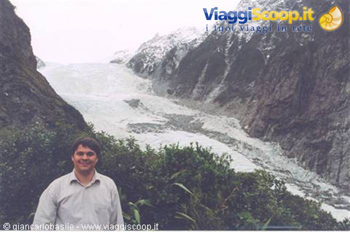 Man in shirt in front of Franz Josef Glacier between snowy rock walls