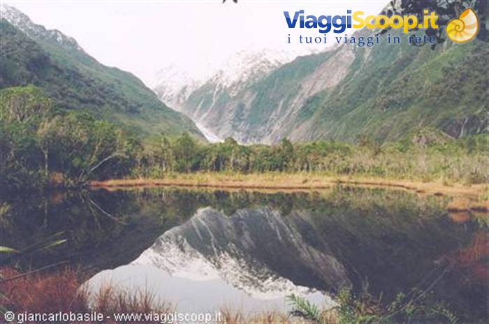 Lake reflecting snowy peaks among forests, Franz Josef Glacier