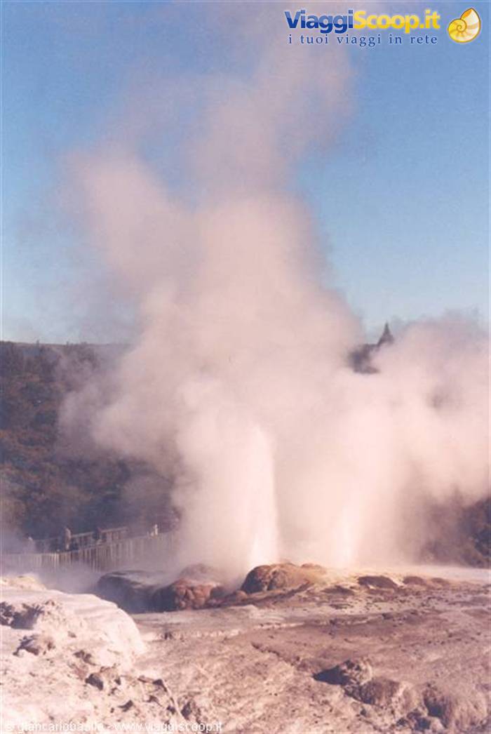 Geyser erupting steam and water over white sinter terraces