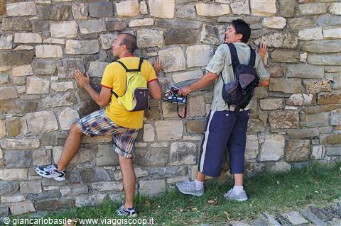 Two tourists with backpacks playfully climbing a dry stone wall