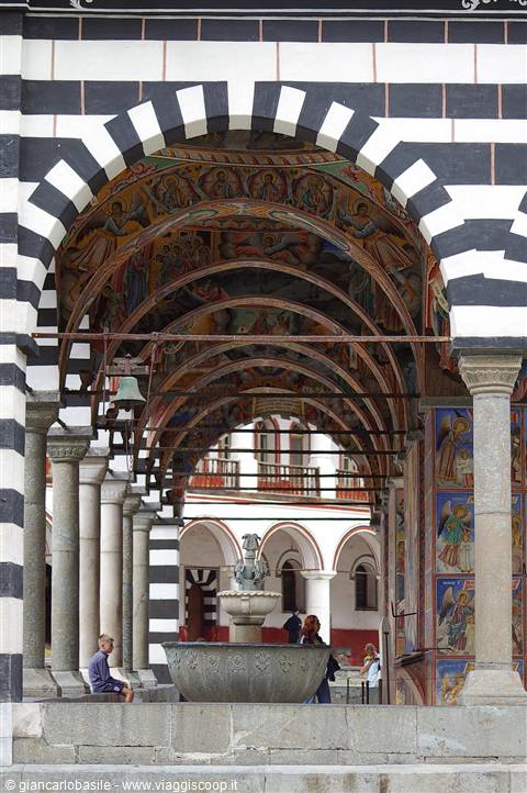 Black-and-white striped arcade with frescoes and fountain, Rila Monastery