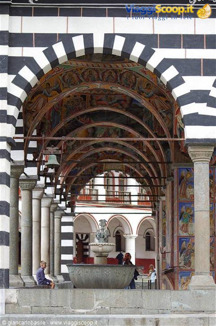 Black-and-white striped arcade with frescoes and fountain, Rila Monastery