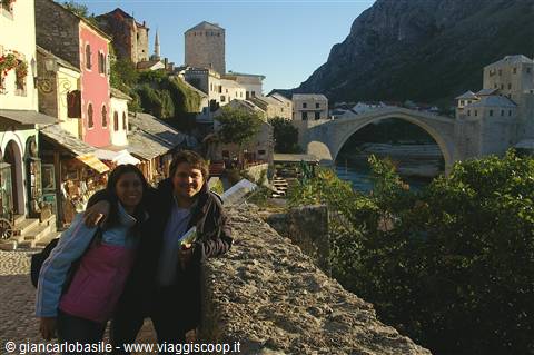 Two smiling women by the stone wall, Mostar's old bridge over the Neretva river