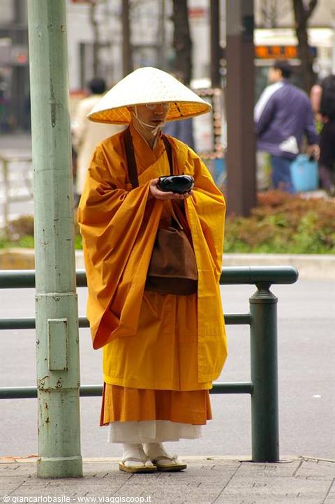 Monk in orange robe and straw hat begging with black bowl on a city street
