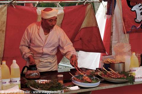 Cook in white headband grilling chicken skewers at a festival food stall