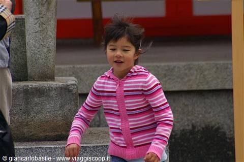 Little girl in pink striped sweater in front of a stone shrine