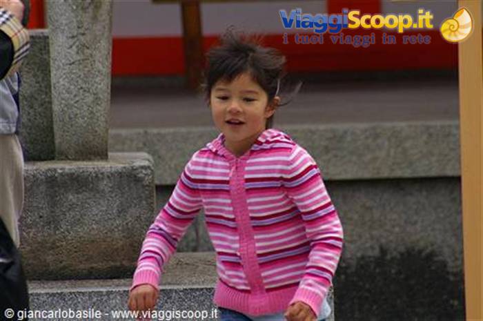Little girl in pink striped sweater in front of a stone shrine