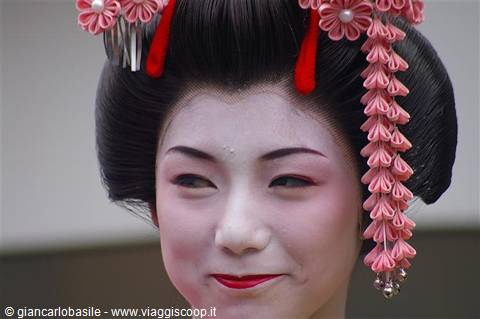 Maiko in white makeup with pink kanzashi flowers in black updo, Kyoto