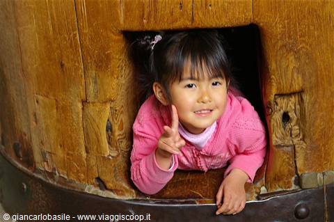 Little girl in pink jacket peeking out of wooden barrel, gesturing