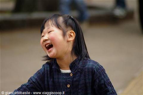 Laughing little girl in blue plaid jacket, dark hair, soft street light