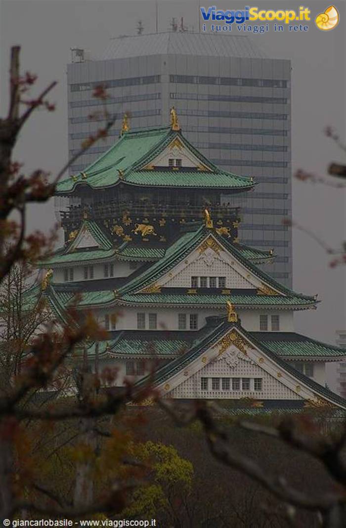 Osaka Castle framed by autumn branches, green roofs and a misty skyscraper