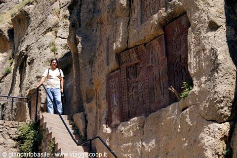 Woman on stone stairs beside khachkar carvings in rock, Geghard monastery