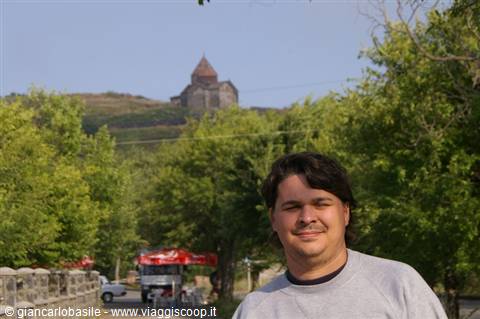 Smiling tourist, behind a medieval stone church on a tree-covered hill