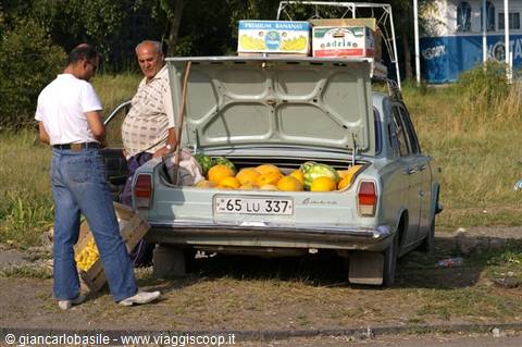 Two men selling melons and watermelons from a car trunk